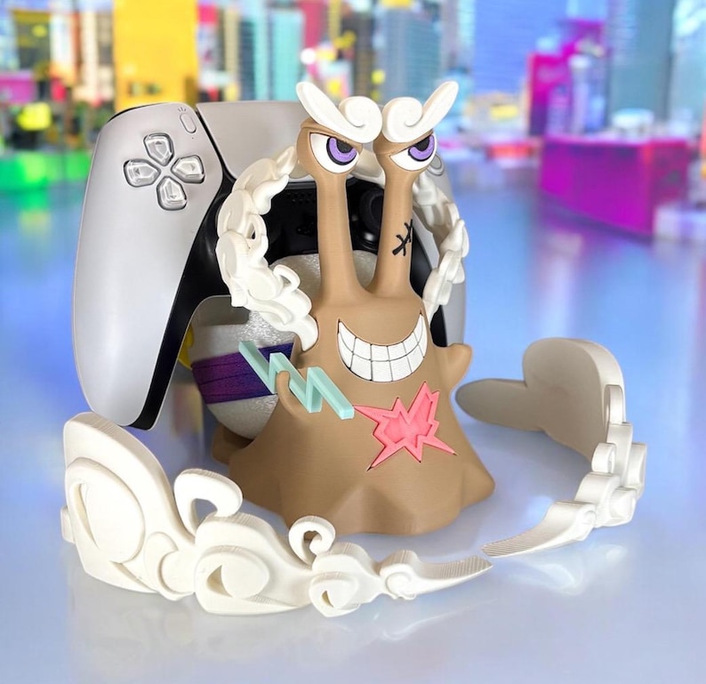 May include: A tan and white figurine of a snail-like character with a wide grin, purple eyes, and white cloud-like accents. The figurine is next to a white and black game controller, with a city backdrop.