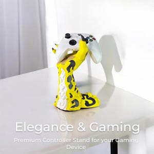 K&ouml;nnte beinhalten: Ein gelber und schwarzer, handf&ouml;rmiger Controller-St&auml;nder mit einem wei&szlig;en Videospiel-Controller, der in der Hand ruht. Der St&auml;nder steht auf einem wei&szlig;en Tisch mit einem schwarzen Metallbein. Der Text "Elegance & Gaming" befindet sich unter dem St&auml;nder, und der Text "Premium Controller Stand for your Gaming Device" befindet sich darunter.
