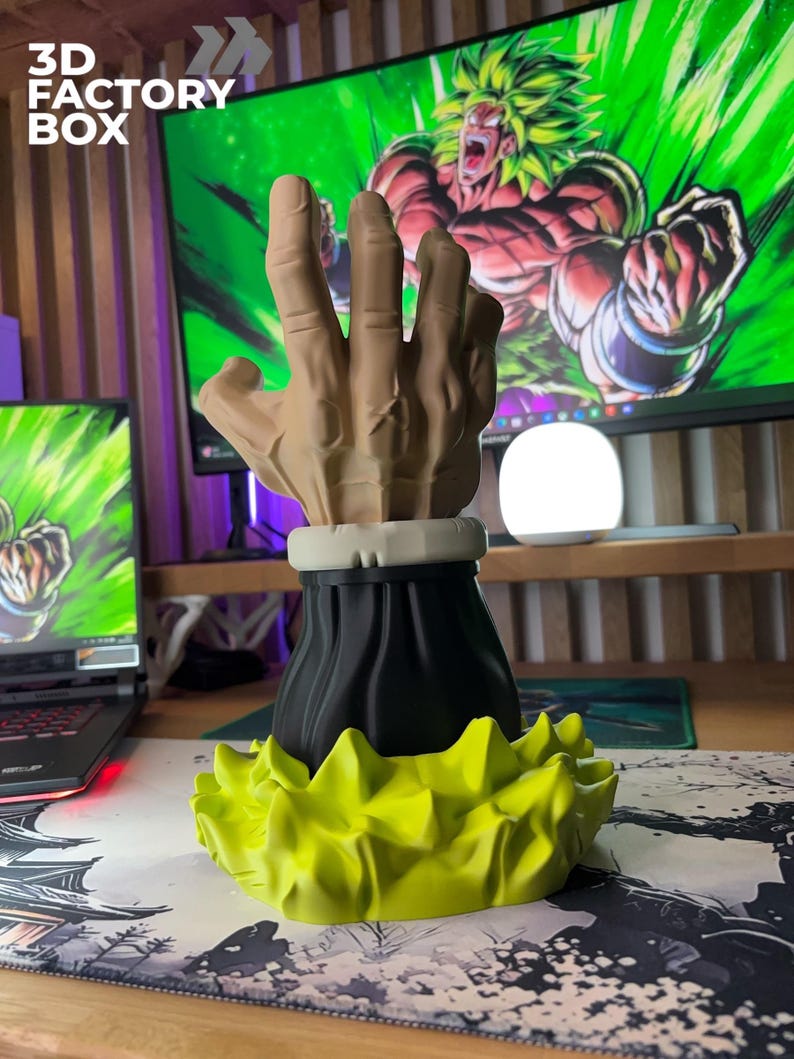 Op de afbeelding: Een 3D-geprinte sculptuur van een hand met een zwarte basis en een geel, stekelig, energie-achtig ontwerp. De hand is beige en lijkt een gebaar te maken. De tekst "3D FACTORY BOX" is zichtbaar in de linkerbovenhoek.