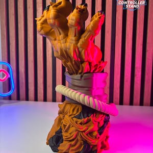 May include: A 3D-printed controller stand in the shape of a tiger's claw. The stand is primarily orange with black accents and a cream-colored rope detail. The text "TIGER CONTROLLER STAND" is visible on the right side of the stand.