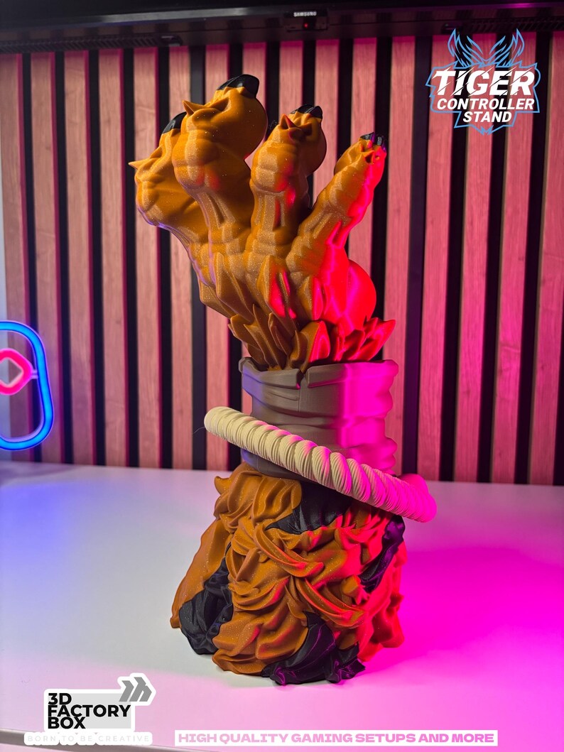 May include: A 3D-printed controller stand in the shape of a tiger's claw. The stand is primarily orange with black accents and a cream-colored rope detail. The text "TIGER CONTROLLER STAND" is visible on the right side of the stand.