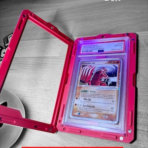 May include: A pink slab case with magnets, holding a Pok&eacute;mon card. The card features a red and white Groudon ex illustration. The case has the text "3D FACTORY BOX" and "Slab Case with Magnets".