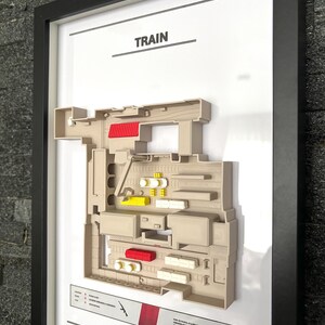 May include: A 3D printed map of the "Train" level from the video game "Counter-Strike: Global Offensive". The map is framed and features a beige color scheme with red and yellow accents. The map is labeled "TRAIN" at the top and includes the "The Factory Box" logo in the bottom right corner.