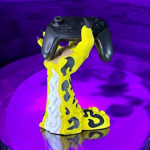 K&ouml;nnte beinhalten: Ein gelber und schwarzer, handf&ouml;rmiger Controller-St&auml;nder mit einem schwarzen Nintendo Switch-Controller in der Hand.