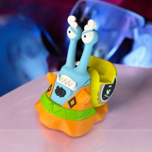 May include: A blue and orange cartoon snail figurine with a yellow shell and a skull and crossbones design. The snail has a toothy grin and large eyes.
