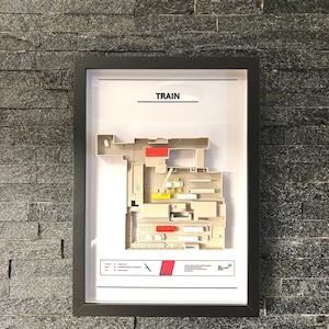May include: A framed black and white diagram of a train layout with the word "TRAIN" at the top. The diagram shows a train track with various buildings and structures along the track. The diagram is in a black frame with a white background.