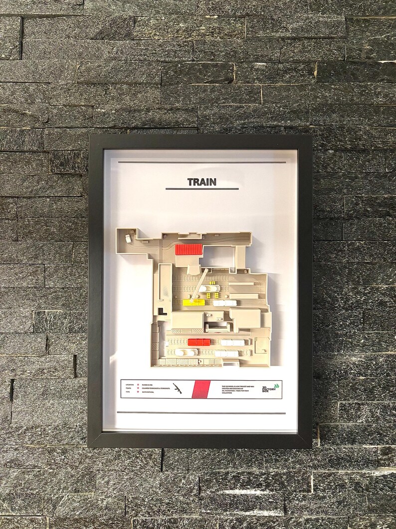 May include: A framed black and white diagram of a train layout with the word "TRAIN" at the top. The diagram shows a train track with various buildings and structures along the track. The diagram is in a black frame with a white background.