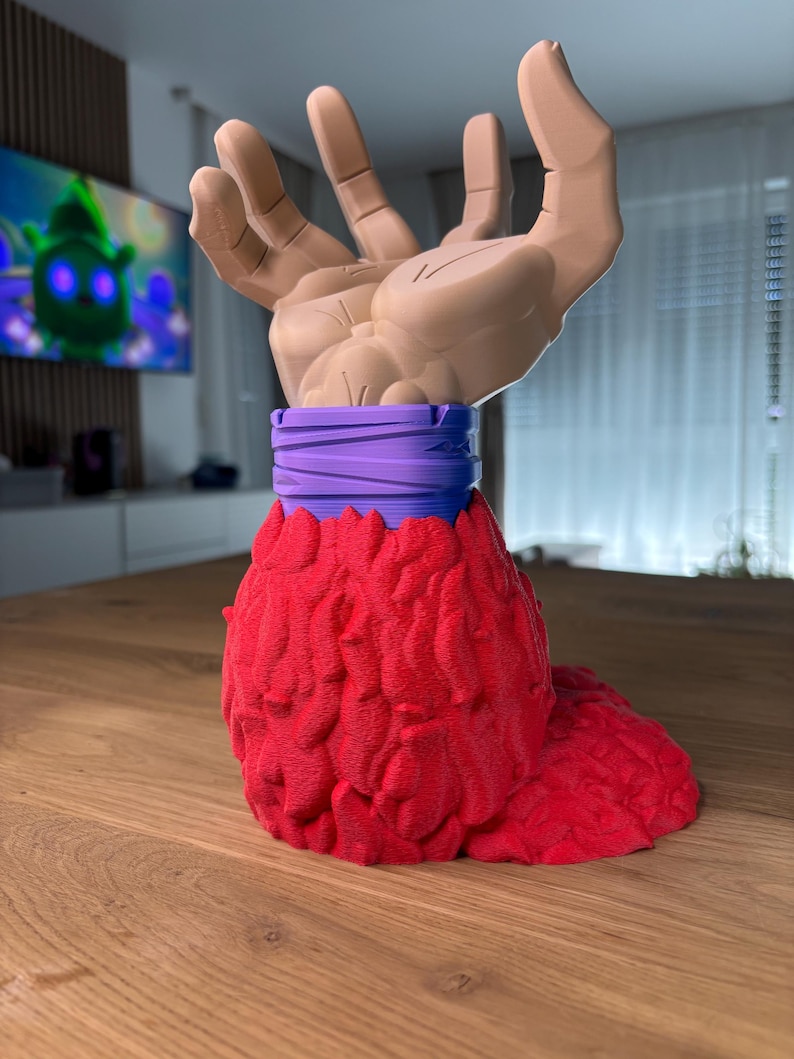May include: A 3D printed figurine of a hand with a red, textured base and a purple band around the wrist.