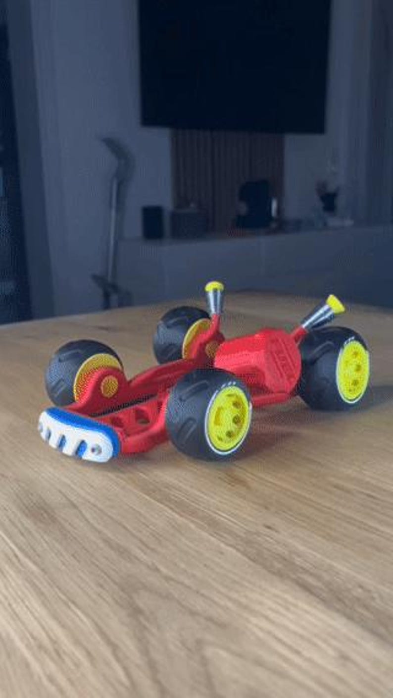 K&ouml;nnte beinhalten: Ein rotes Spielzeug-Rennauto mit schwarzen Reifen und gelben Felgen. Der vordere Sto&szlig;f&auml;nger ist wei&szlig; und blau. Das Auto hat gelbe Akzente und steht auf einer Holzoberfl&auml;che.