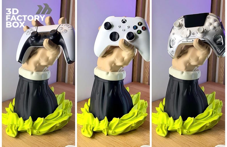 Op de afbeelding: Een 3D-geprinte gamecontrollerhouder met een hand die een wit-zwarte PlayStation 5-controller, een witte Xbox-controller en een zilveren controller vasthoudt. De basis is zwart met een witte kraag en een groen bladontwerp.
