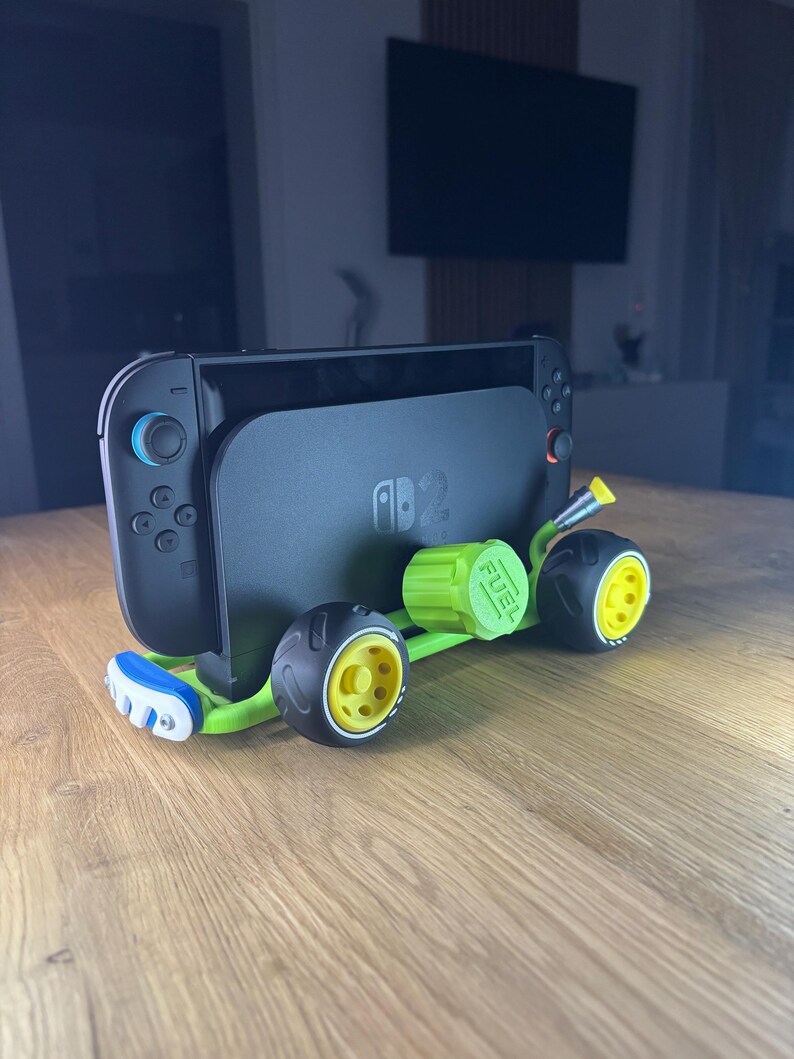 K&ouml;nnte beinhalten: Eine schwarze Nintendo Switch-Konsole ist auf einem gr&uuml;n-gelben 3D-gedruckten Spielzeugauto-Chassis montiert. Das Auto hat schwarze R&auml;der mit gelben Zentren und einen gr&uuml;nen Tankdeckel. Auf dem Bildschirm der Konsole ist das Nintendo-Logo zu sehen.