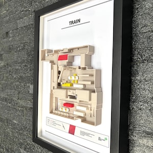 May include: A white framed print with a 3D model of a train. The title of the print is "TRAIN". The print is on a gray stone wall.