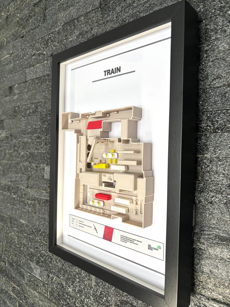 May include: A white framed print with a 3D model of a train. The title of the print is "TRAIN". The print is on a gray stone wall.