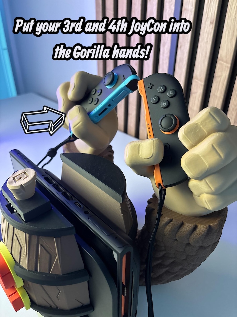 May include: A gaming accessory featuring a gorilla hand design holding two Joy-Con controllers. The text reads, "Put your 3rd and 4th JoyCon into the Gorilla hands!" The controllers are black and blue.