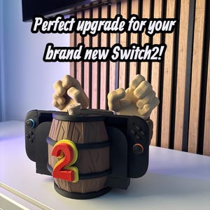 May include: A black Nintendo Switch controller dock with a brown barrel design and the number 2 in red and yellow. The text reads "Perfect upgrade for your brand new Switch2!"