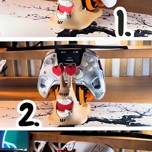May include: A whimsical, tan-colored controller stand shaped like a cartoon snail with red heart-shaped eyes. The stand holds a white Xbox controller. The snail has a wide, toothy grin and orange accents.