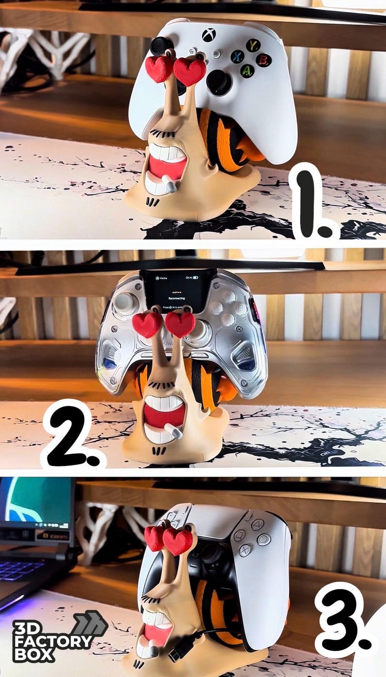 May include: A whimsical, tan-colored controller stand shaped like a cartoon snail with red heart-shaped eyes. The stand holds a white Xbox controller. The snail has a wide, toothy grin and orange accents.