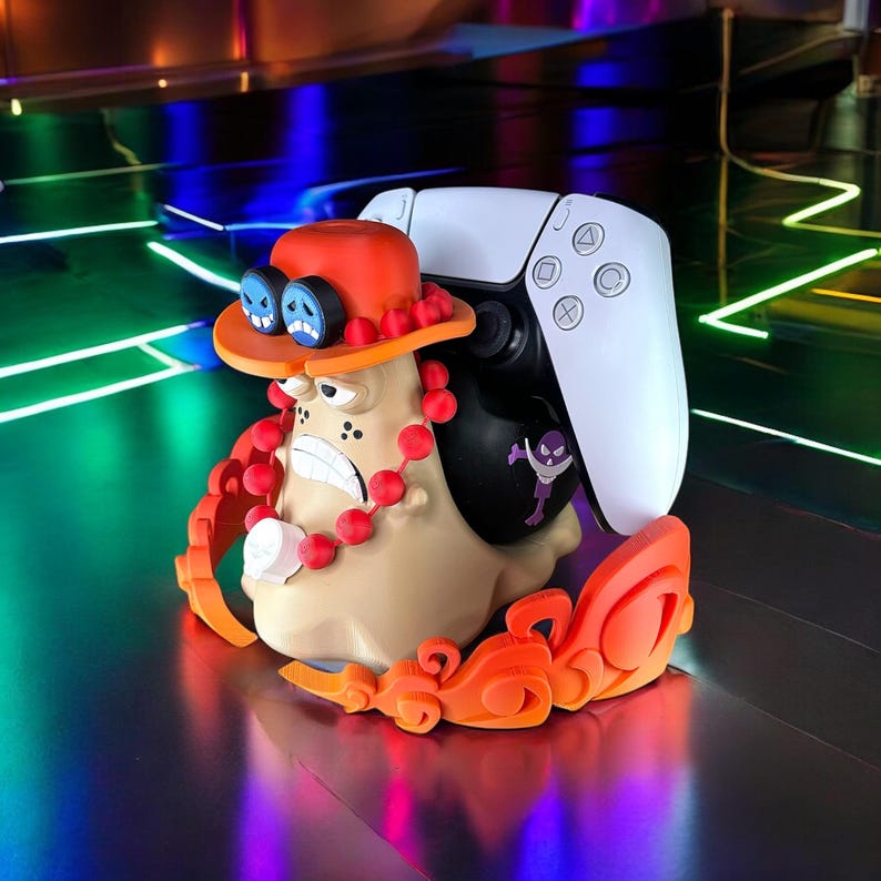 Peut inclure: Un support d'impression 3D pour une manette de jeu vid&eacute;o, avec un personnage de dessin anim&eacute; portant un chapeau rouge et une manette blanche et noire.