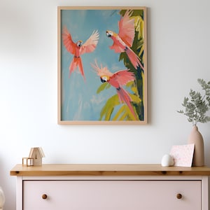 K&ouml;nnte beinhalten: Ein gerahmtes Gem&auml;lde mit drei rosa Papageien, die in einem blauen Himmel mit gr&uuml;nen Palmenbl&auml;ttern fliegen. Die Papageien haben gelbe Schn&auml;bel und schwarze Augen.