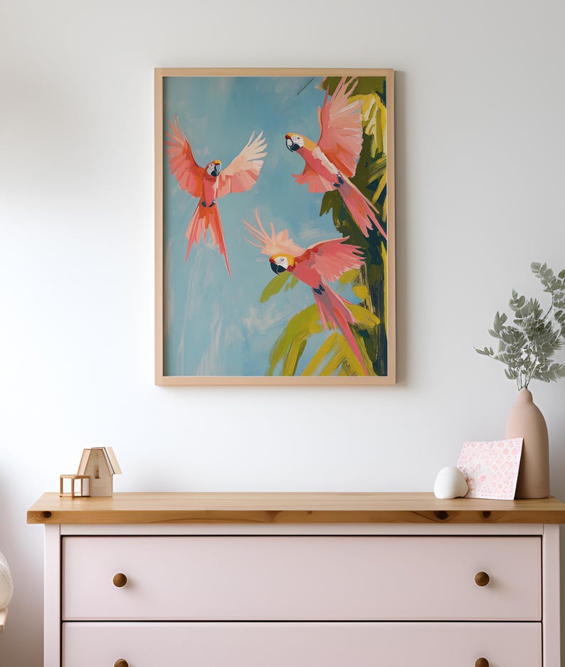 K&ouml;nnte beinhalten: Ein gerahmtes Gem&auml;lde mit drei rosa Papageien, die in einem blauen Himmel mit gr&uuml;nen Palmenbl&auml;ttern fliegen. Die Papageien haben gelbe Schn&auml;bel und schwarze Augen.