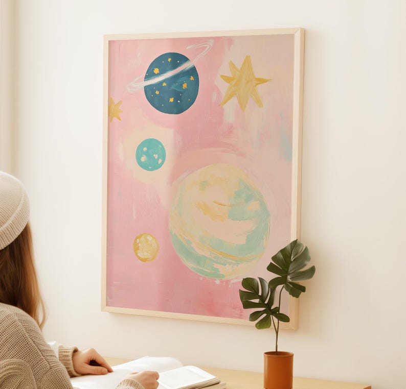 May include: A pink and blue abstract painting of planets and stars. The painting is framed in a light wood frame.