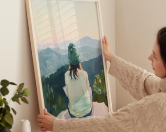 May include: A framed painting of a person wearing a green beanie sitting on a rock overlooking a mountain range. The painting is in a light wood frame.