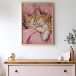 Op de afbeelding: Twee oranje tabby-katten knuffelen en slapen in een roze deken met witte stippen.