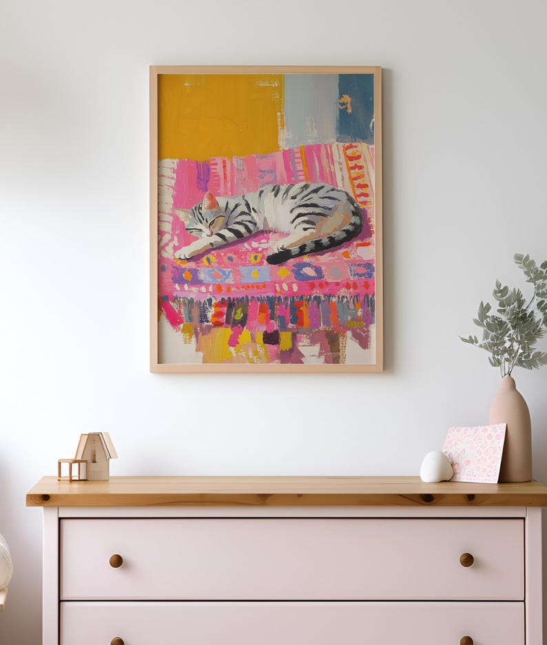 May include: A framed painting of a gray and white cat sleeping on a colorful rug. The rug has pink, yellow, blue, and green stripes and patterns. The background is a white wall.