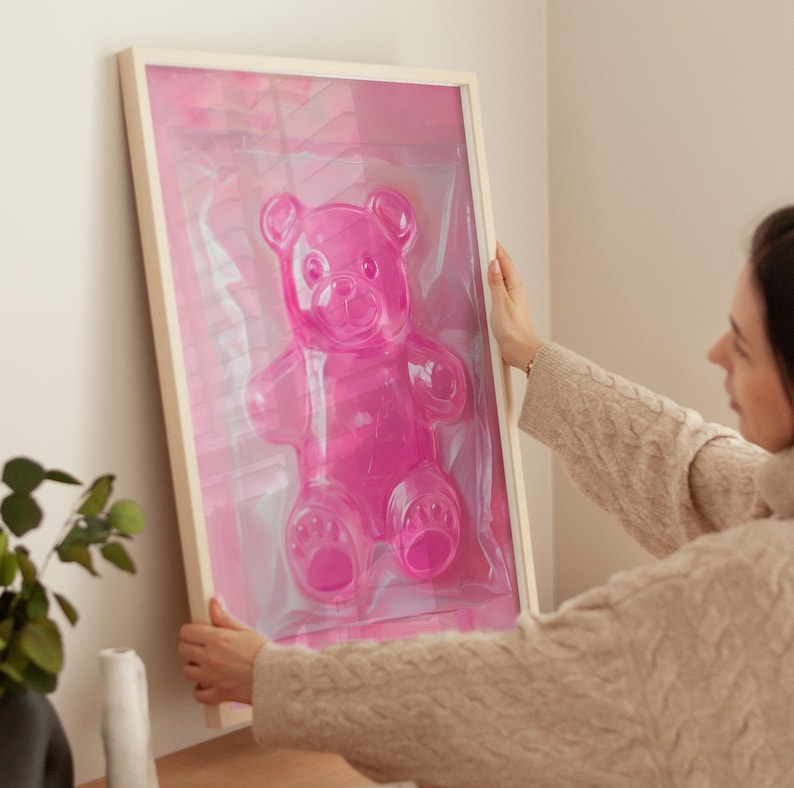 May include: A framed pink gummy bear sculpture in a clear plastic bag. The sculpture is in a wooden frame with a white mount.