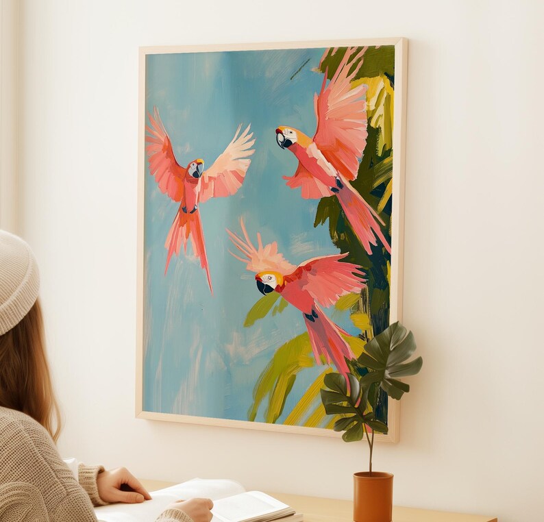 K&ouml;nnte beinhalten: Ein Gem&auml;lde von drei rosa und gelben Aras, die vor einem blauen Himmel und gr&uuml;nen Palmenbl&auml;ttern fliegen.
