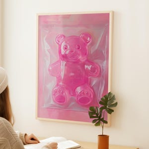 May include: A framed pink gummy bear sculpture in a clear plastic bag. The bear is in a pink frame with a white mount.