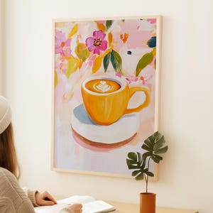 May include: A framed art print of a yellow coffee cup with latte art on a white saucer. The background features a floral design with pink, yellow, and green brushstrokes. The artwork is displayed on a white wall.