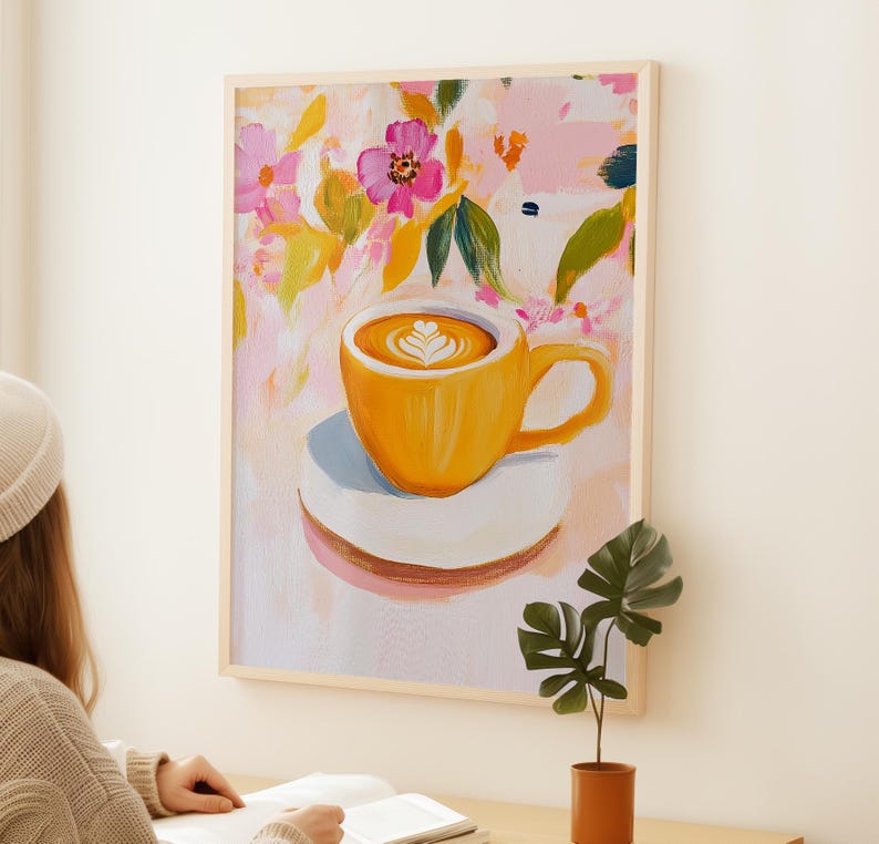 May include: A framed art print of a yellow coffee cup with latte art on a white saucer. The background features a floral design with pink, yellow, and green brushstrokes. The artwork is displayed on a white wall.