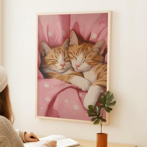 Op de afbeelding: Twee oranje tabby-katten knuffelen onder een roze deken met witte stippen. De katten slapen met hun ogen dicht.