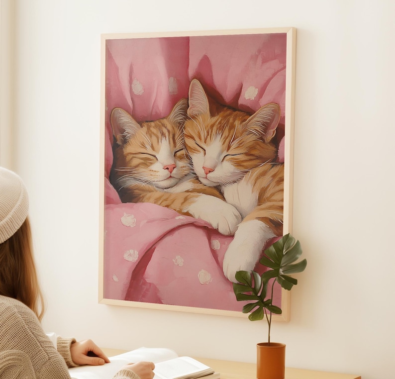 Op de afbeelding: Twee oranje tabby-katten knuffelen onder een roze deken met witte stippen. De katten slapen met hun ogen dicht.