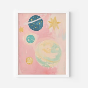 May include: A pink and blue abstract painting with a white frame. The painting features a blue planet with a ring around it, a yellow star, and several smaller planets in a galaxy-like design.