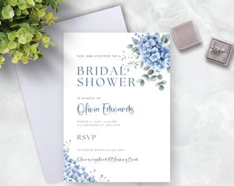 May include: A blue and white bridal shower invitation with watercolour flowers and the text "You are invited to a Bridal Shower in honour of Olivia Edwards. March 15, 2023 at 1:00 PM. 123 Anywhere St, Any City. RSVP to Ashley Phone 121-454-2890. Olivia is registered at Blushing Bride."