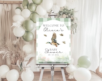 Könnte beinhalten: Ein grünes und weißes kariertes Willkommens-Schild für eine Babyparty. Das Schild zeigt eine Aquarell-Illustration eines fliegenden Entchens mit dem Text "Willkommen zur Babyparty von Olivia 08.10.2023".