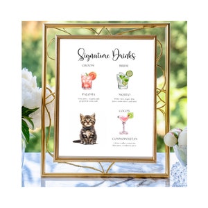 May include: A gold-framed sign with the text "Signature Drinks" and illustrations of cocktails. The groom's drink is a Paloma, the bride's drink is a Mojito, and the couple's drink is a Cosmopolitan. A cute kitten is pictured below the groom's drink.