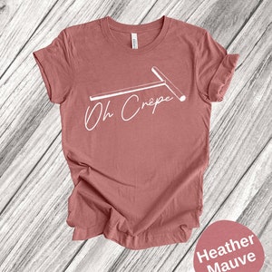 May include: A heather mauve t-shirt with a white graphic of a crepe maker and the text "Oh Cr&ecirc;pe".