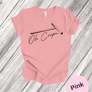 May include: Pink t-shirt with a black graphic of a crepe maker and the text "Oh Cr&ecirc;pe".