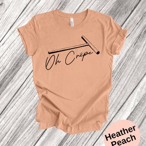May include: A heather peach t-shirt with a black graphic of a crepe maker and the text "Oh Cr&ecirc;pe".