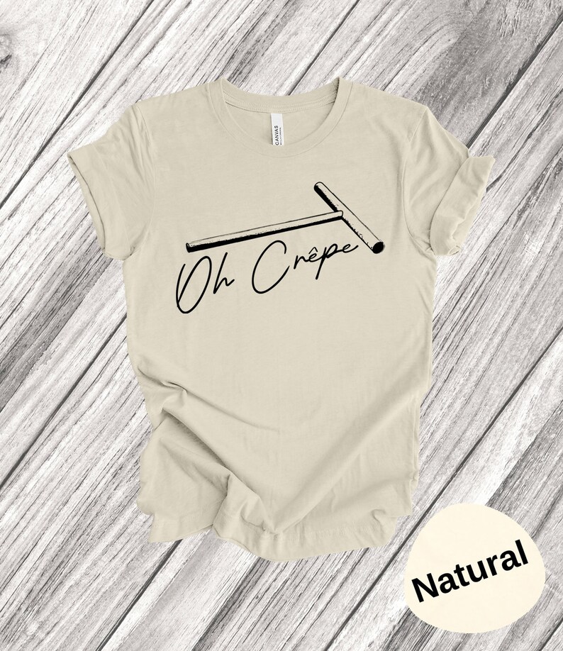 May include: A beige t-shirt with a black graphic of a crepe maker and the text "Oh Cr&ecirc;pe". The shirt is on a wooden background. The colour of the shirt is "Natural".