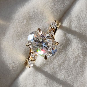 May include: A gold engagement ring featuring an oval-shaped diamond and smaller diamonds set in the band.