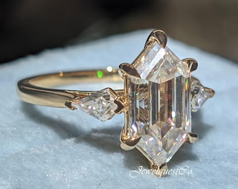 May include: A gold ring with a large, clear, octagonal-shaped diamond in the center. Two smaller, clear, pear-shaped diamonds are set on either side of the center stone. The ring is in a blue velvet box.
