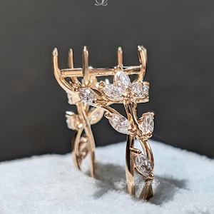 May include: A rose gold ring setting with a floral design. The ring features marquise-cut stones set in a leaf-like pattern, with prongs ready to hold a center stone. The ring is displayed on a white surface.