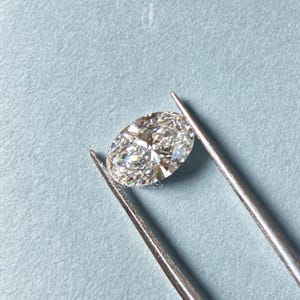 Loose oval cut diamond displayed against a light blue background, showcasing pristine clarity and cut symmetry, crafted in lab conditions to provide a sustainable and affordable alternative to mined diamonds.