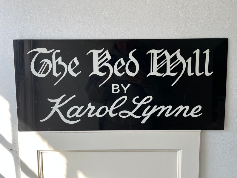 Op de afbeelding: Een zwart-wit bord met de tekst "The Bed Mill by Karol Lynne" in een cursief schrift.
