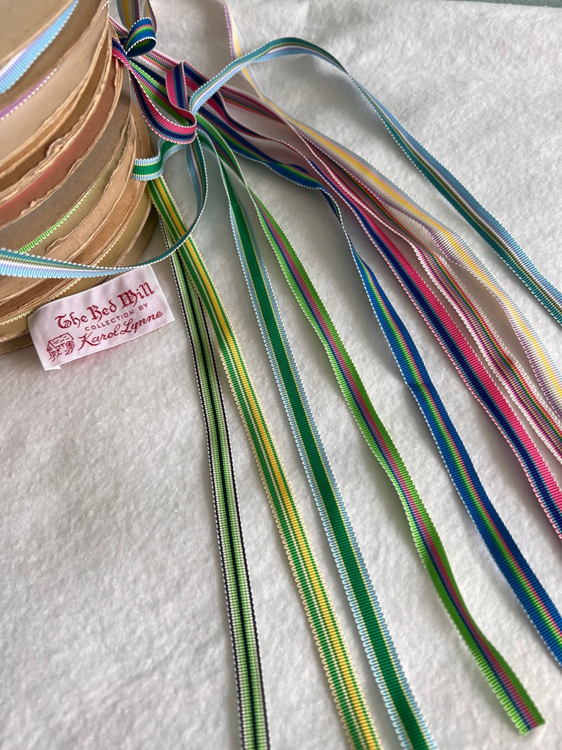 Op de afbeelding: Assortiment van kleurrijke gestreepte lintrollen met een label met de tekst "The Red Mill Collection by Karol Lynne".