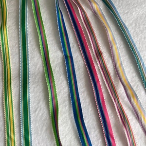 Op de afbeelding: Assortiment van kleurrijke gestreepte linten in verschillende kleuren, waaronder groen, blauw, roze, geel en wit.